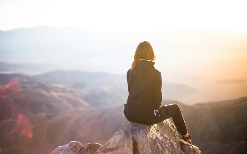 A woman sits on a rock above a misty mountain valley at sunrise.