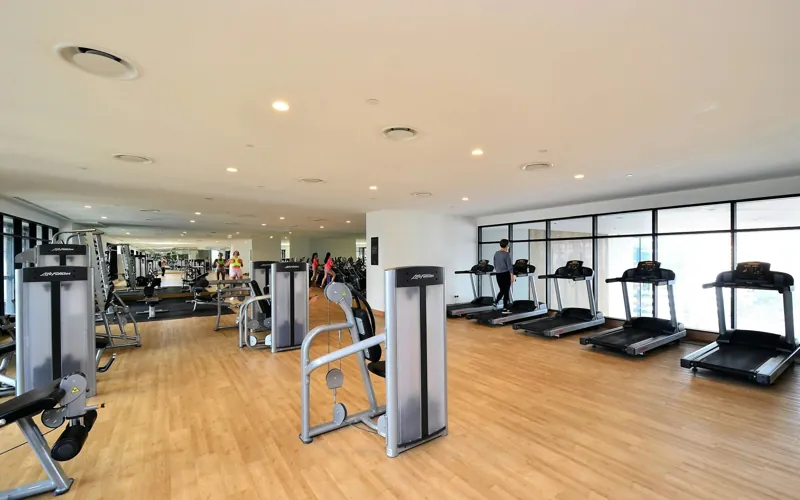 A bright fitness center with rows of treadmills and strength machines on a wood floor.